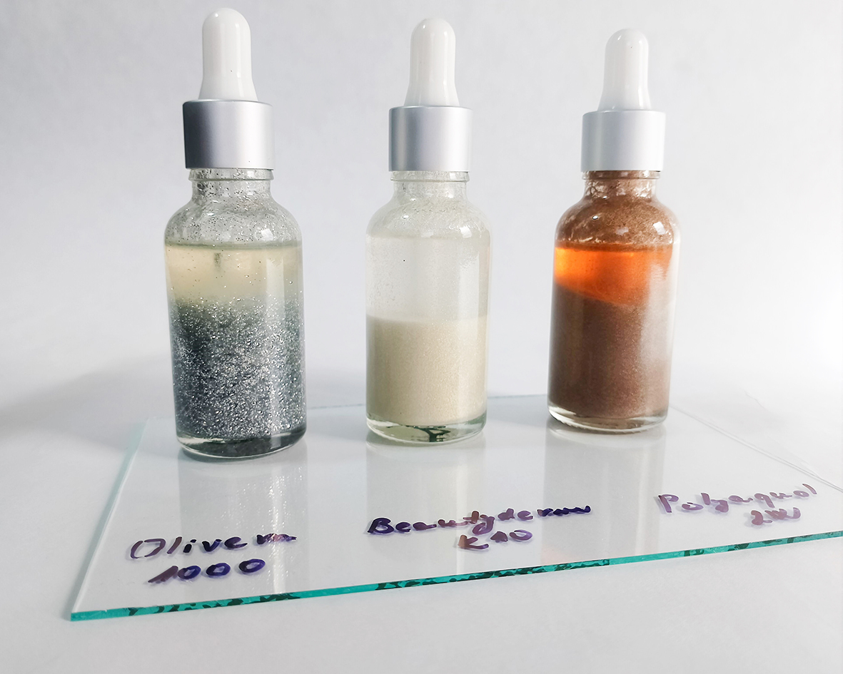 Tri typy trblietavého telového oleja v sklenených fľaškách s kvapkátkom na bielom pozadí.